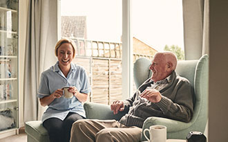 Elderly man sitting in chair laughing with middle aged woman sitting beside him on ottoman