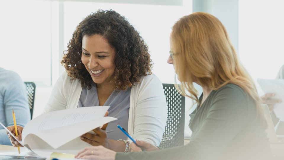 Smiling woman files through stack of paper with team member