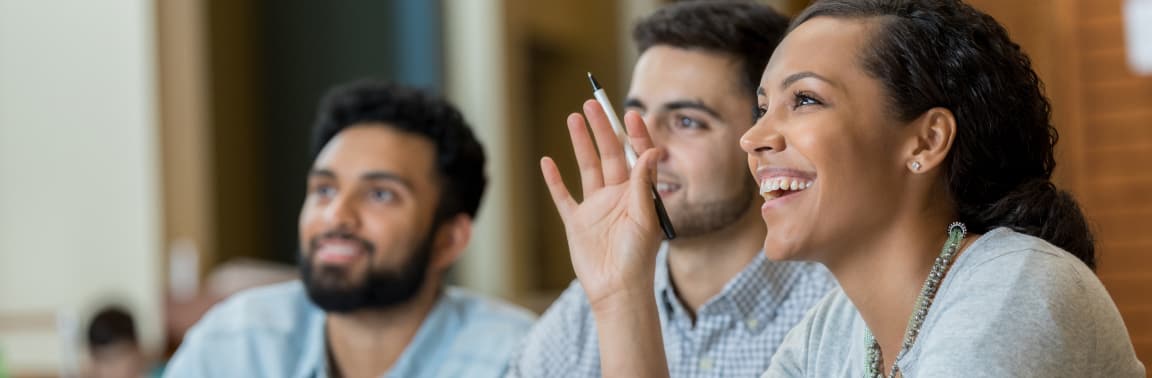 Woman close to frame smiling and raising her hand, while coworkers look on