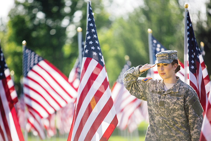 A female soldier in uniform saluting the American flag in an outdoor setting.