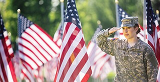 A female soldier in uniform saluting the American flag in an outdoor setting.