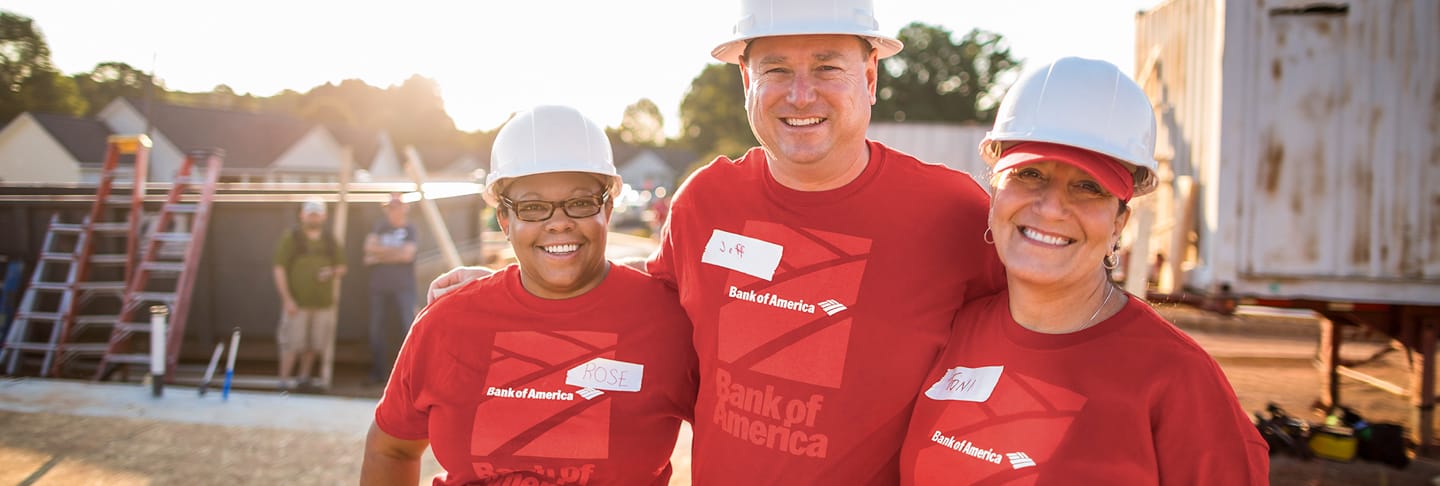 Three employees in hard hats and red t-shirts embracing and smiling for camera