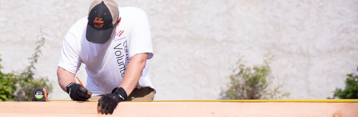 Man volunteering measures planks of wood outside