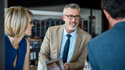 Older man in tan jacket talking to colleagues