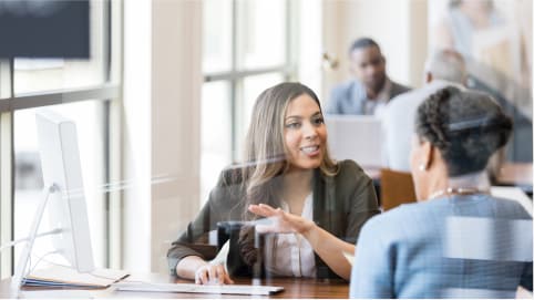 A bank attendant helps a customer while sitting in a sunny office space