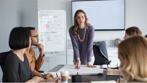 Woman leaning over a conference table while seated team listens