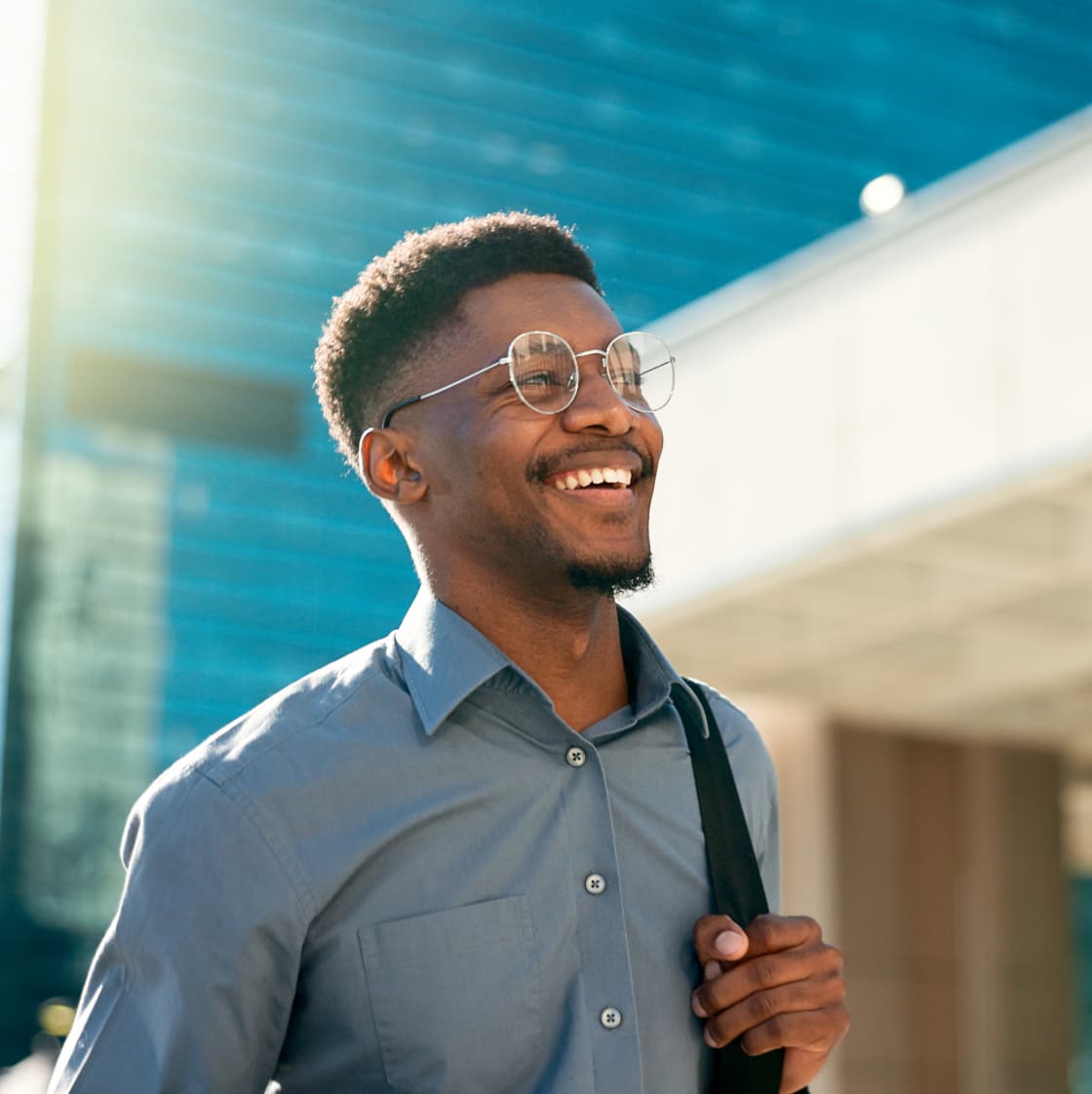 Smiling, confident male employee wearing a laptop bag, walking to work on a sunny day